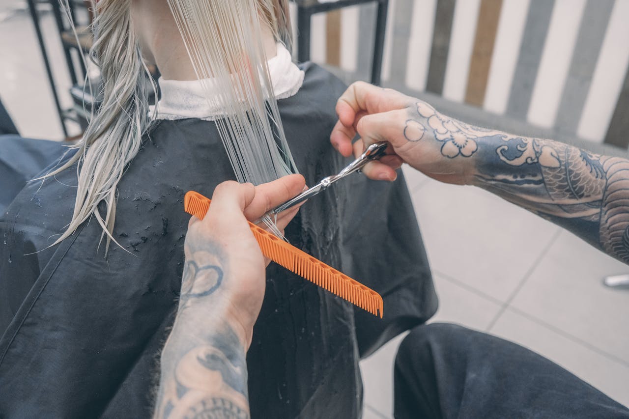 Close-up of a stylists tattooed hands cutting wet hair in a modern beauty salon.