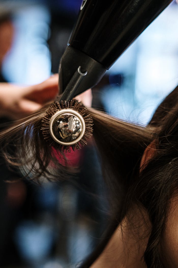 Close-up of a hairstylist styling hair with a brush and dryer in a salon setting.